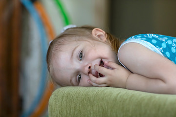 Little cheerful girl is lying on the sofa in the room. Emotional portrait.