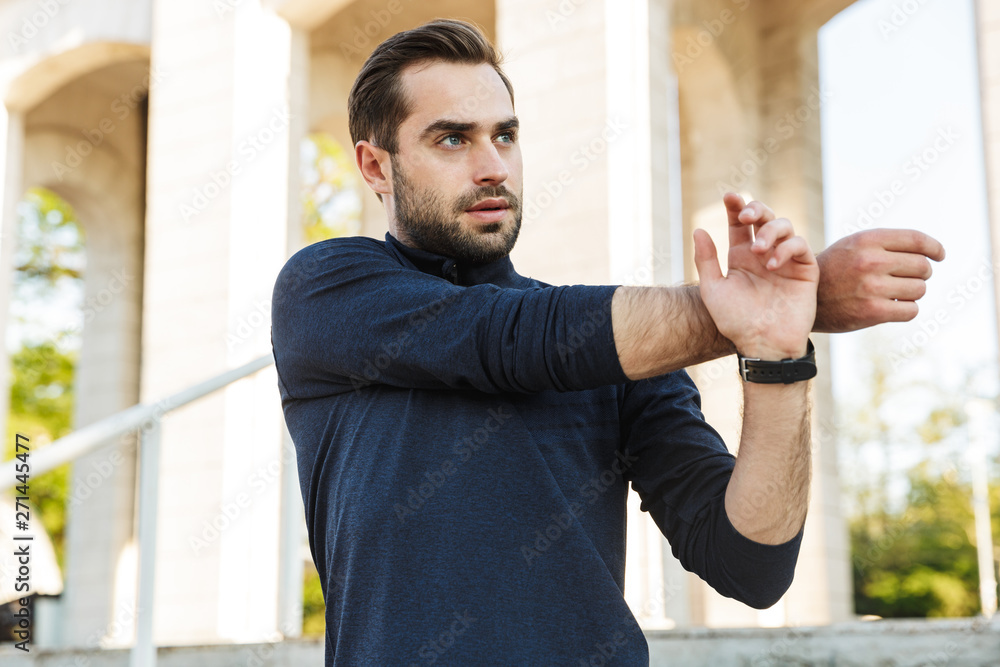 Wall mural Handsome young strong sports man posing outdoors at the nature park location make stretching exercises.