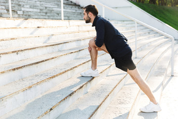 Handsome young strong sports man posing outdoors at the nature park location make stretching...
