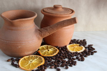 Turk and milk jug, made of clay dishes, a lot of roasted coffee bean and dried orange. composition, selective focus