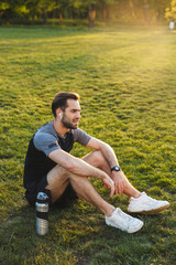 Handsome young strong sports man posing outdoors at the nature park location resting sitting...