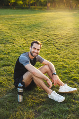 Handsome young strong sports man posing outdoors at the nature park location resting sitting...