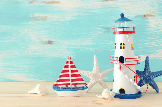 vacation and summer concept with vintage boat, starfish, lighthouse and seashells over wooden table or shelf infront of pastel blue background