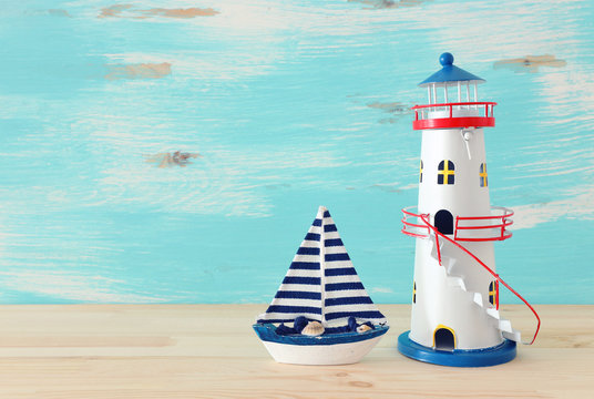 vacation and summer concept with vintage boat and lighthouse over wooden table or shelf infront of pastel blue background