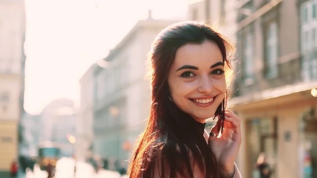 happy pretty girl in city goes smiling to camera toch hair wind sunshine background