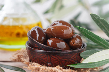 Delicatessen Greek Kalamata black red glossy olives in ceramic bowl on wooden table. Oil and twigs. Selective focus
