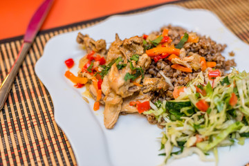 Pieces of rabbit stew with pepper, onion and herbs with boiled buckwheat and salad of fresh vegetables cucumbers and cabbage on a white plate. Mouth-watering delicious food at the gala dinner