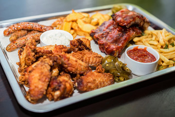 Dish of mixed meats. Grilled ribs, chicken wings and sausages with French fries