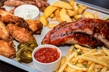 Dish of mixed meats. Grilled ribs, chicken wings and sausages with French fries