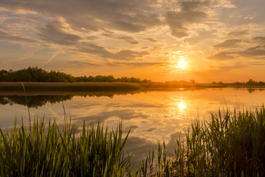 Sunset above the pond or lake with cloudy sky at summer and water reflection.