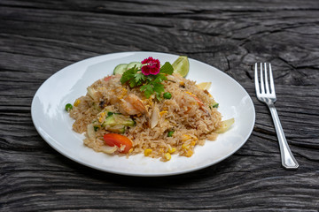 Fried rice with shrimps and vegetables in a white dish on an old wooden table, close up . Thai food...