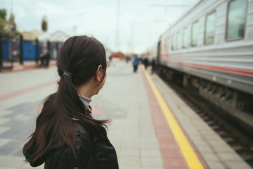 Young woman waiting for arrival of train. Side view unrecognizable young brunette female standing...