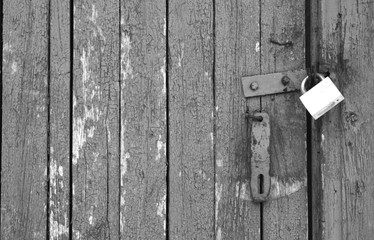 Old padlock on wooden gate in black and white.