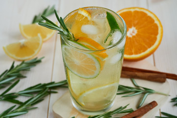 a glass of cool lemonade with citrus fruits and rosemary, cinnamon on a wooden table