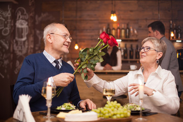 Woman in her sixties happy to recieve roses from her husband during dinner