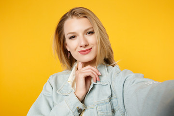 Close up selfie shot of attractive smiling young woman in denim casual clothes looking camera isolated on bright yellow orange wall background in studio. People lifestyle concept. Mock up copy space.