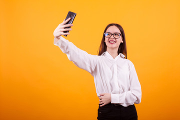 Naklejka premium Pretty teenage girl taking a selfie and smiling to the camera over yellow background