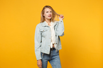 Portrait of pensive beautiful young woman in denim casual clothes looking up and holding hair isolated on bright yellow orange wall background in studio. People lifestyle concept. Mock up copy space.