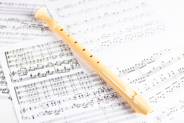 Plastic beige flute on sheets with musical notes