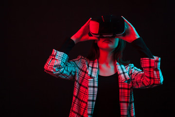 Beautiful young girl using modern virtual technology in studio over black background with colored light