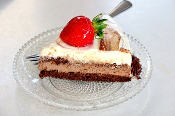 a slice of cake of three different layers with strawberries on a small plate