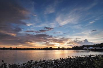 Lake view evening of dark clouds moving above reservoir with yellow sun light and cloudy sky background, sunset at Krajub Reservoir, attraction in Ban Pong, Ratchaburi, Thailand.