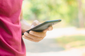 close up handsome man use left hand typing mobile phones and touch screen working with app devices in park with sunrise and green blur nature background.
