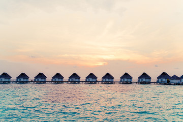 Beautiful tropical sunset over Maldives island with water bungalow in hotel resort