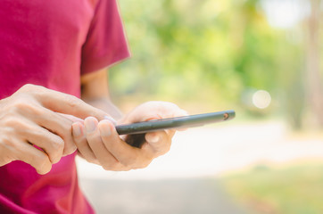 close up handsome man use left hand typing mobile phones and touch screen working with app devices in park with sunrise and green blur nature background.