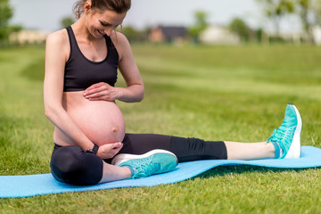 Pregnant woman fitness exercises on grass at sunny day