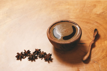 Black coffee in wooden cup with wooden spoon and star anise on wooden background. Copy-space and author processing.