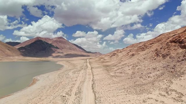 Aerial over gravel off road trail near arid desert mountains in sunny day.Pamir highway silk road trip adventure in Kyrgyzstan and Tajikistan desert,central Asia.4k drone flight establisher video
