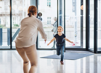 A rear view of businesswoman greeting with small daughter in office building.