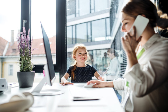 A businesswoman with small daughter sitting in an office, working.