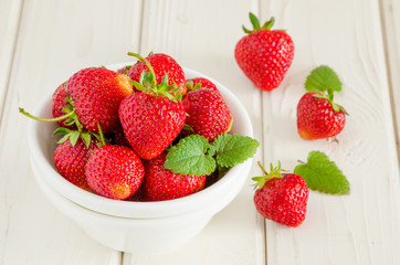 Fresh ripe strawberries in a bowl on a white wooden background.