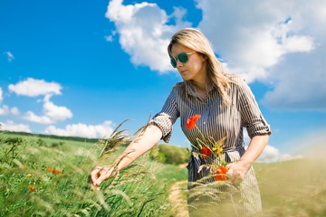 A woman is plucking a poppy picking a bouquet of wildflowers.