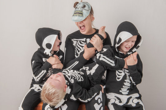 Happy friendly family of musicians in carnival costumes, boys and young mother play together. Black suit with image of skeletons. Classic halloween costume. Funny children
