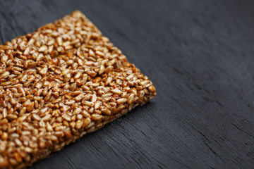 Tile kozinaki from sunflower seeds on a black textural background. Delicious oriental sweets Gozinaki from sunflower seeds, sesame seeds and peanuts, covered with honey with a shiny icing