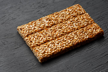 Tile kozinaki from sunflower seeds on a black textural background. Delicious oriental sweets Gozinaki from sunflower seeds, sesame seeds and peanuts, covered with honey with a shiny icing