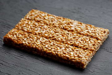 Tile kozinaki from sunflower seeds on a black textural background. Delicious oriental sweets Gozinaki from sunflower seeds, sesame seeds and peanuts, covered with honey with a shiny icing