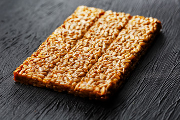 Tile kozinaki from sunflower seeds on a black textural background. Delicious oriental sweets Gozinaki from sunflower seeds, sesame seeds and peanuts, covered with honey with a shiny icing