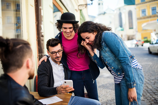 A Group Of Young Friends With Smartphone Sitting In An Outdoor Cafe, Talking.