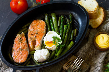 Salmon fish steak grilled with asparagus, poached egg in a frying pan on a rustic stone table. Healthy food. Top view flat lay.
