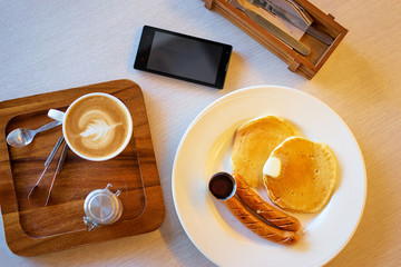 Smart phone on table during breakfast. Copy space on screen. Top view scene with food and coffee.