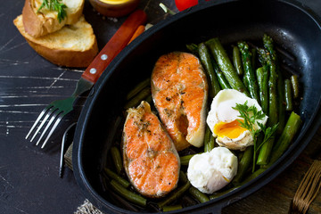 Salmon fish steak grilled with asparagus, poached egg in a frying pan on a rustic stone table. Healthy food. Top view flat lay.
