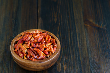 Dried bird's eye chili peppers in a wooden bowl. Dark wooden table, high resolution, negative space