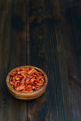 Dried bird's eye chili peppers in a wooden bowl. Dark wooden table, high resolution, negative space