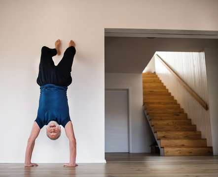 A Senior Man Indoors At Home, Doing Handstand Exercise Indoors.