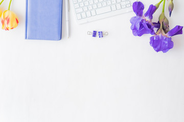Flat lay blogger or freelancer workspace with a notebook, keyboard, yellow tulips and blue irises on a white background