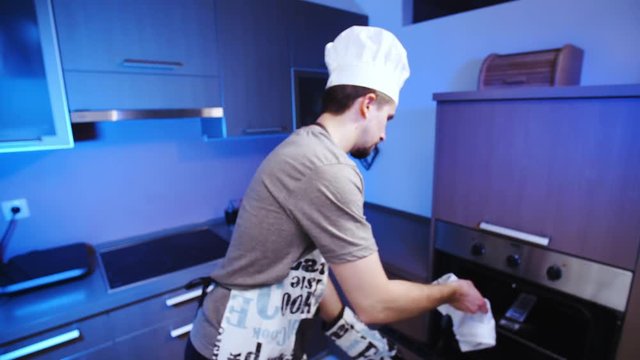 Cook baking bullshit in oven 4K. Wide view close-up on person face and dish in focus, smiling into the camera with kitchen in the background out of focus.